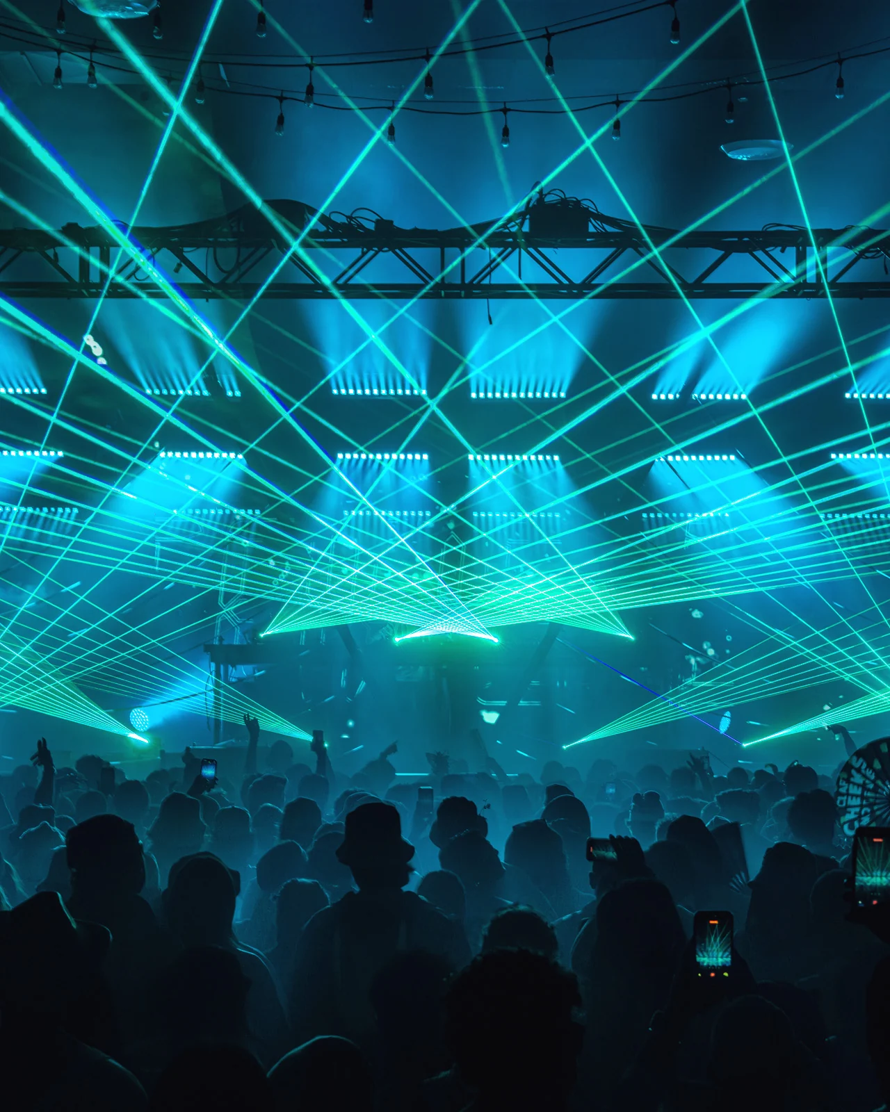 Cyan laser beams crisscrossing above a silhouetted crowd