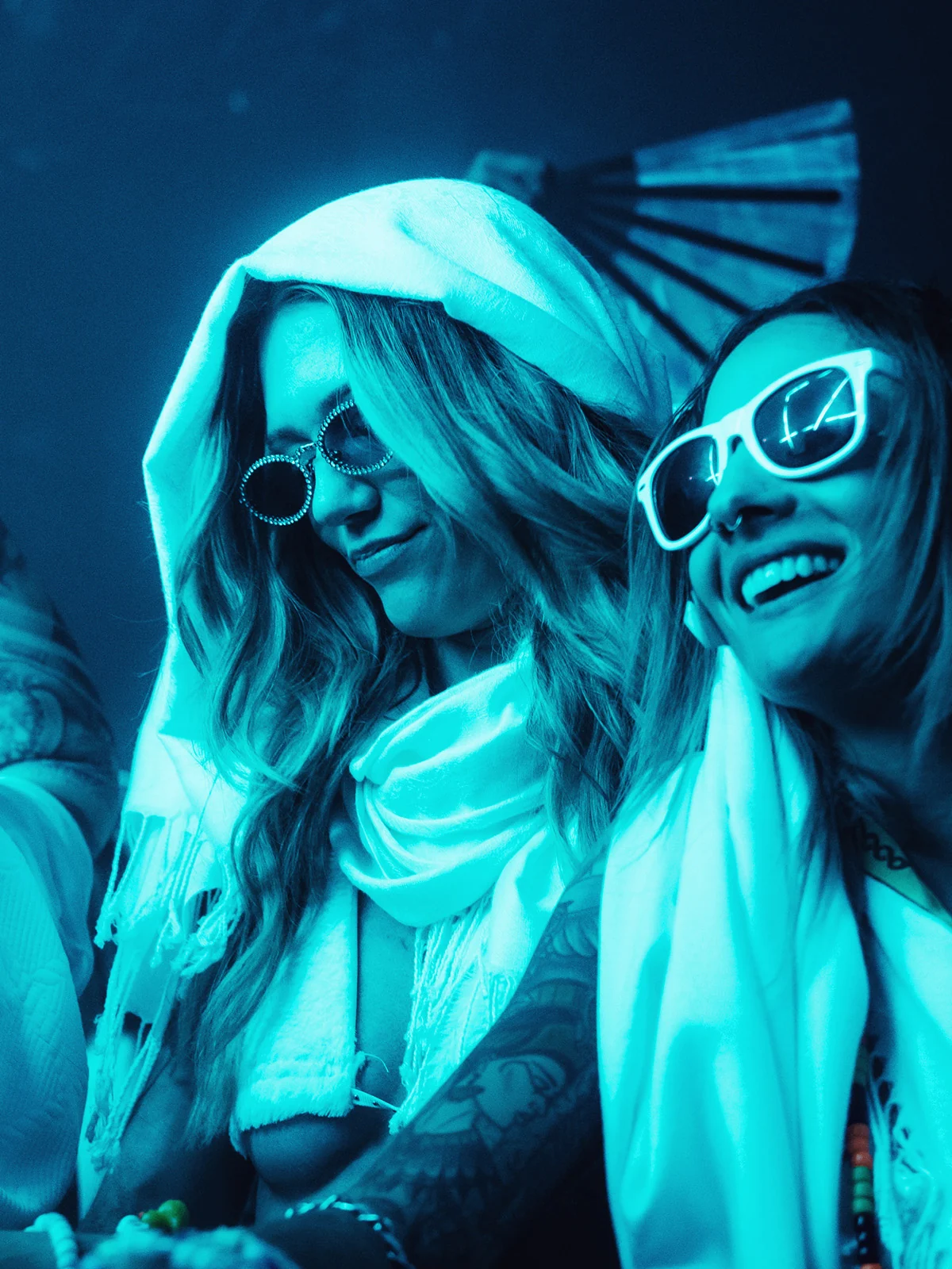 Two guests in sunglasses and white hoods lit in cyan